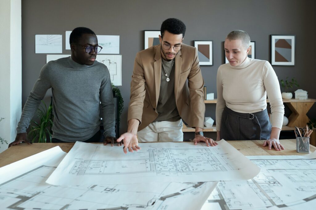One of three coworkers making presentation of large sketch on blueprint